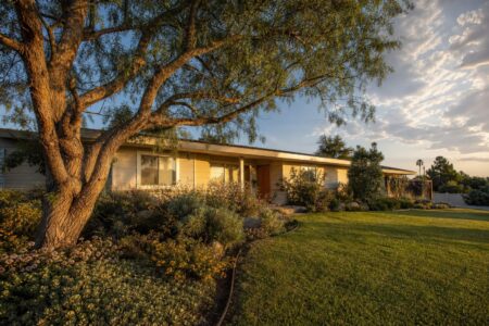 Single-story 1960s ranch home with cream siding, low roofline, and mature pepper tree on spacious front lawn in Mesa Del Mar, Costa Mesa.