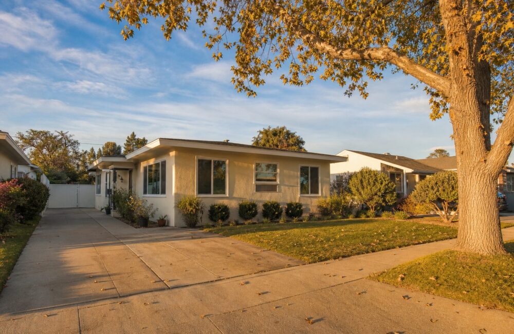 Original 1954 stucco bungalow with mature tree and wide driveway in Westside Costa Mesa's Freedom Tract.