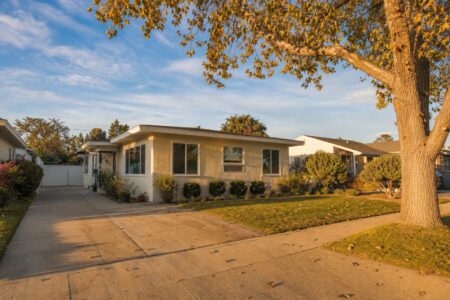 Original 1954 stucco bungalow with mature tree and wide driveway in Westside Costa Mesa's Freedom Tract.
