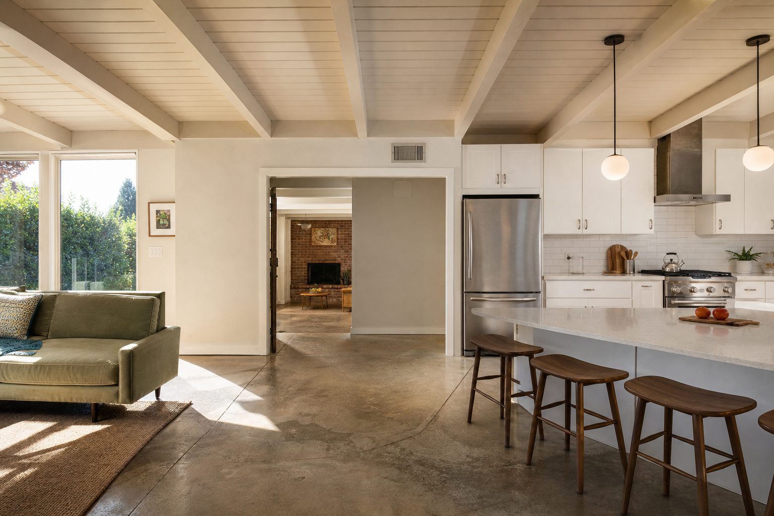 Open kitchen-family room with exposed wood beams, modern appliances, and natural light in renovated 1960s ranch home interior.